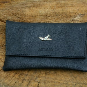 May include: A black leather wallet with a flap closure. The wallet has a small airplane pin on the front and the word "ARTAMIS" embossed on the front.