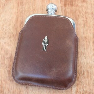 May include: A brown leather flask with a silver top and a small silver figure of a person wearing a suit and tie.