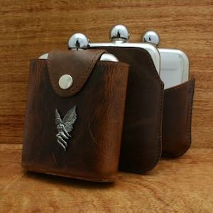 Peut inclure: Trois flacons d'alcool en argent avec des étuis en cuir marron. L'étui du plus grand flacon a un motif de fée en argent.