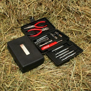 May include: A black plastic toolbox with a variety of tools, including screwdrivers, pliers, and a socket wrench. The toolbox is open and the tools are visible. The toolbox is sitting on a bed of hay.