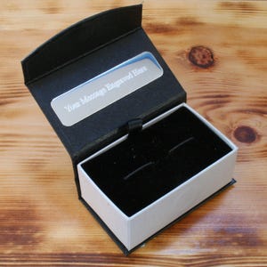 May include: A black cufflink box with a white interior and a silver plate on the top that says "Your message engraved here".
