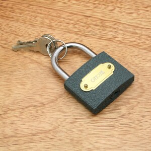 May include: A gray padlock with a brass keyhole and a brass nameplate that reads "CHRIS". The padlock is attached to a silver key.