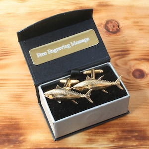 Peut inclure: Boutons de manchette en or en forme de deux thons, présentés dans un coffret cadeau noir avec une doublure argentée. Le coffret est doté d'une plaque dorée sur laquelle est inscrit "Message de gravure gratuit".