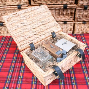 May include: A wicker basket with a lid, filled with a glass, a wooden box, a metal flask, and whiskey stones. The flask has a dinosaur design and the glass has a lizard design.