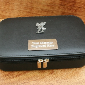 Puede incluir: Estuche de viaje negro con cremallera, un amuleto de hada plateado y una placa plateada que dice "Su mensaje grabado aquí".