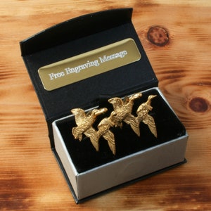 May include: A black gift box with a silver interior, containing four gold-colored flying duck cufflinks. The box has a gold plaque that reads "Free Engraving Message".