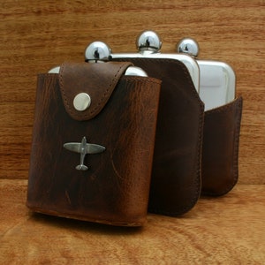 May include: Three brown leather hip flasks with silver tops. The flask on the left has a small silver airplane charm.