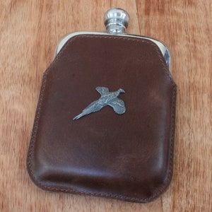 May include: A brown leather flask with a silver pheasant design on the front.