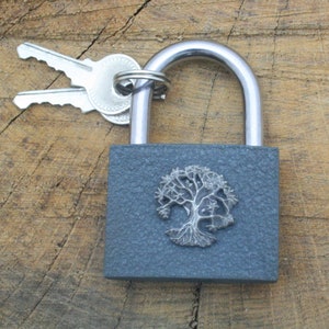 May include: A gray padlock with a silver tree of life design. The padlock is attached to two silver keys.