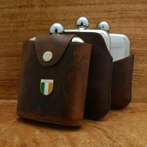 May include: Three silver hip flasks with brown leather cases. The case of the flask on the left has a small green, white, and orange Irish flag emblem with the word "IRELAND" printed on it.