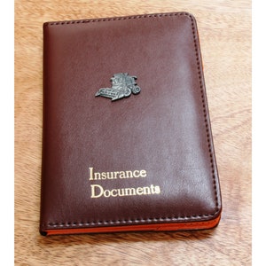 May include: A brown leather insurance document holder with a metal combine harvester emblem and the words "Insurance Documents" in gold lettering.