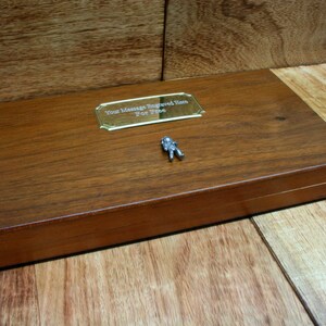 May include: A wooden box with a brass plaque that says "Your Message Engraved Here For Free". There is a small astronaut figurine on the box.