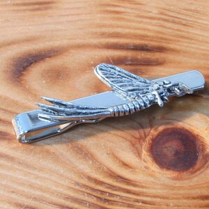 May include: Silver tie clip featuring a detailed design of a mayfly insect.