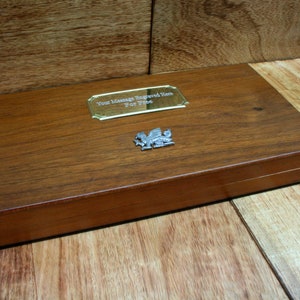 May include: A wooden box with a brass plaque that says "Your Message Engraved Here For Free". The box has a silver dragon emblem on the lid.