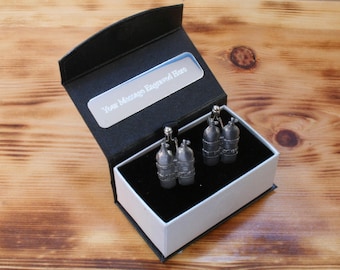 May include: A black gift box with a white interior and a silver plaque that reads "Your Message Engraved Here." Inside are silver-colored cufflinks shaped like diving tanks. The box sits on a wooden surface.