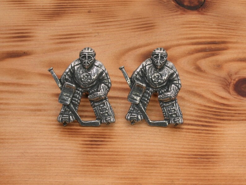 Pu&ograve; includere: Un paio di gemelli argentati con un portiere di hockey in azione. Il portiere indossa un casco e delle protezioni, e tiene un bastone da hockey. I gemelli sono un ottimo regalo per gli appassionati di hockey.