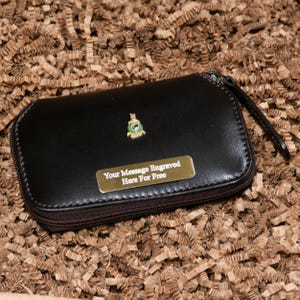 May include: A brown leather zipped case with a gold metal plate that says "Your Message Engraved Here For Free". The case has a green and gold emblem on the front.