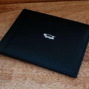 Könnte beinhalten: Eine schwarze Lederbörse mit einem silbernen Flugzeug-Anhänger.