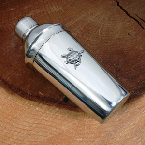 May include: A silver cocktail shaker with a turtle design on the side.