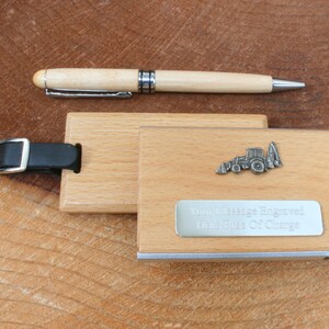 May include: A wooden luggage tag with a metal tractor charm and a silver plate that reads "Your Message Engraved Here New Set Of Change". The tag has a black leather strap with a silver buckle. A wooden pen is also included.