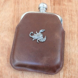 May include: A brown leather flask with a silver scorpion design on the front.
