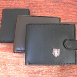 May include: Three leather wallets in black, brown, and dark brown. The largest wallet has a small metal emblem with a lion design.