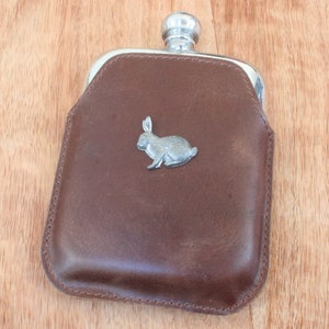 May include: A brown leather flask with a silver rabbit design.