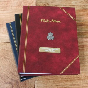 Könnte beinhalten: Drei Fotoalben übereinander gestapelt. Das obere Album ist rot mit goldenen Verzierungen und dem Text "Photo Album" geprägt auf der Vorderseite. Das mittlere Album ist schwarz mit goldenen Verzierungen. Das untere Album ist blau mit goldenen Verzierungen.