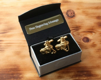May include: A black gift box with a silver lining, containing a pair of gold cufflinks. The cufflinks are shaped like a pair of skis and ski poles. The box has a gold plaque that says "Free Engraving Message".