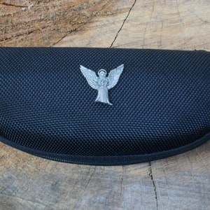 Puede incluir: Estuche negro para gafas con cremallera y un dije de ángel plateado unido al tirador de la cremallera.