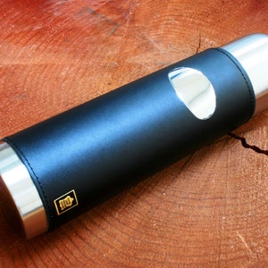 Peut inclure: Une thermos en acier inoxydable recouverte de cuir noir avec un accent argenté et un petit logo doré.
