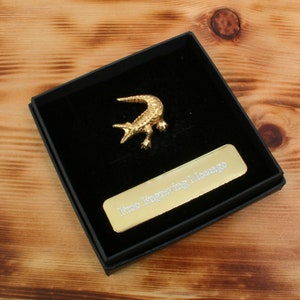 Pode incluir: Uma figura de jacaré dourada em uma caixa de veludo preto com uma placa dourada que diz "Three Inspiring Messages".