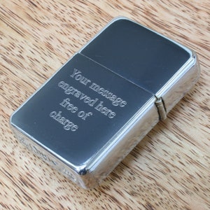 May include: A silver lighter with a black insert. The lighter has an inscription that reads "Your message engraved here free of charge".