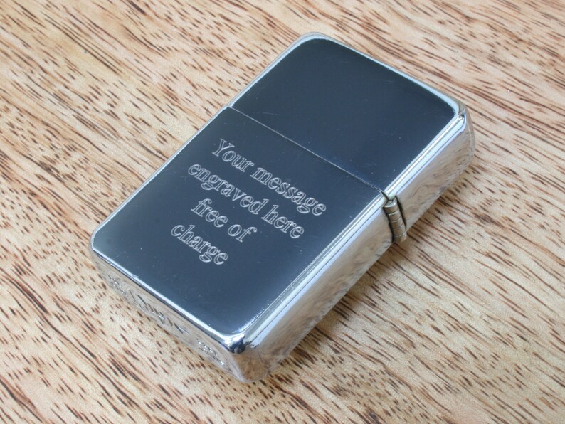 May include: A silver lighter with a black insert. The lighter has an inscription that reads "Your message engraved here free of charge".