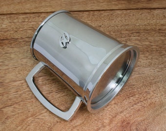 May include: A silver metal beer stein with a handle. The stein has a raised design on the front.