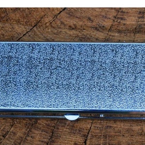 May include: A silver metal rectangular box with a textured surface. The box has a hinged lid and a small latch.