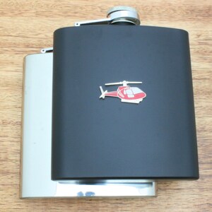Pode incluir: Uma garrafa de bolso de aço inoxidável preta com uma tampa prateada e um design de helicóptero vermelho.