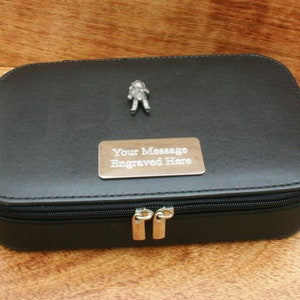Puede incluir: Estuche de viaje negro con cremallera, con un dije de astronauta plateado y una placa plateada que dice "Su mensaje grabado aquí".