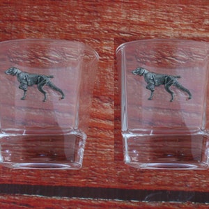 May include: Two clear glass shot glasses with a silver German Shorthaired Pointer dog design on the front.
