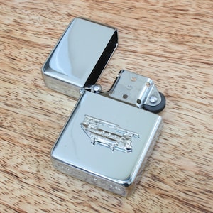 Könnte beinhalten: Ein silberner Feuerzeug mit Chromoberfläche und einer detaillierten Gravur eines Doppeldeckerbusses auf der Vorderseite.