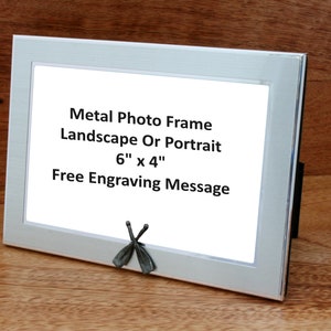 Puede incluir: Marco de fotos de metal plateado con un paspartú blanco y un frente de vidrio transparente. El marco mide 15,24 cm por 10,16 cm y se puede usar para fotos de paisaje o retrato. El marco tiene una opción de mensaje de grabado gratuito. El marco está sobre una superficie de madera.