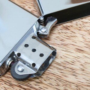 May include: A silver lighter with a black wheel and a silver hinge. The lighter is open and the wheel is visible.