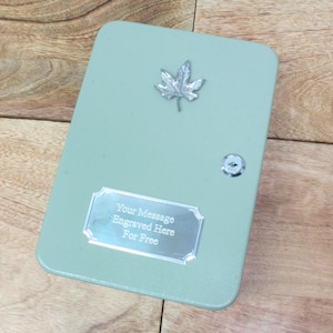 May include: A light green metal box with a silver maple leaf design and a silver plaque that says "Your Message Engraved Here For Free".
