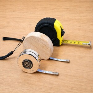 Könnte beinhalten: Drei Maßbänder auf einer Holzoberfläche. Eines ist schwarz und gelb, ein anderes aus Holz und das dritte silberfarben mit einem Kompassdesign. Das gelbe Maßband erstreckt sich bis zu 20 cm.