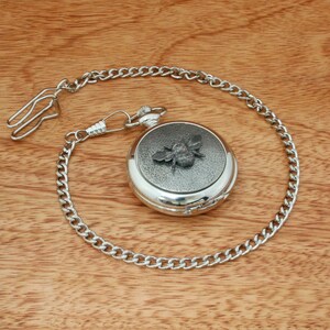 May include: Silver pocket watch with a bee design on the face and a silver chain.