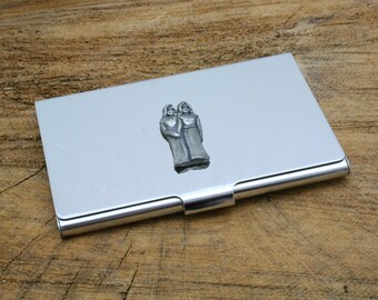 May include: A silver metal business card holder with a pewter design of two people standing together.