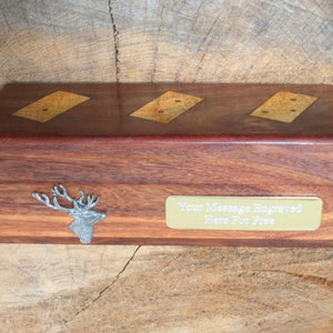 Puede incluir: Una caja de madera con una placa de latón que dice "Su mensaje grabado aquí gratis". La caja tiene tres dominós incrustados en la parte superior y un ciervo de plata en la parte delantera.