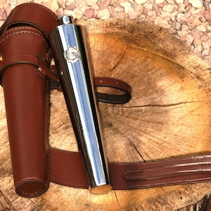 May include: A silver hip flask with a brown leather carrying case and strap. The flask has a decorative design on the front.
