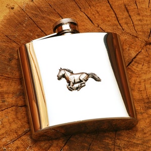 Può includere: Una fiaschetta d'argento con un design di cavallo al galoppo.