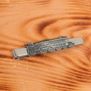 May include: A silver tie clip featuring a detailed model of a vintage steam locomotive.